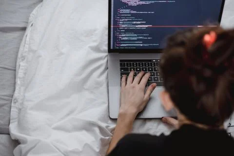 Young female programmer writes program code on a computer laptop in the bed . Photos
