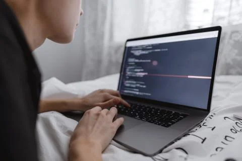 Young female programmer writes program code on a computer laptop in the bed . Stock Photos