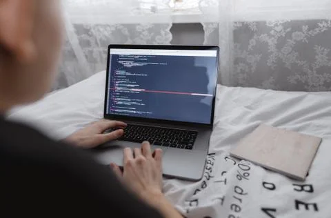 Young female programmer writes program code on a computer laptop in the bed . Stock Photos
