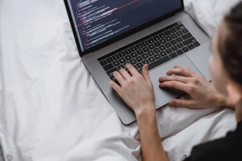 Young female programmer writes program code on a computer laptop in the bed . Photos