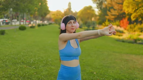 Young female runner stretching arms before fitness workout in the park. Видео 342597560