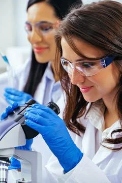 Young female scientist using microscope while her colleague working in Stock Photos