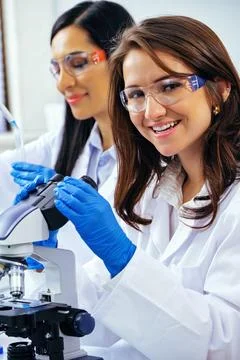 Young female scientist using microscope while her colleague working in Stock Photos