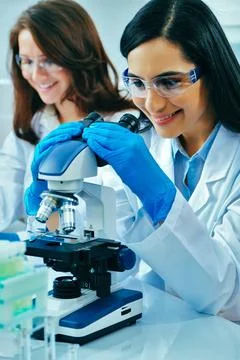 Young female scientist using microscope while her colleague working in Foto stock