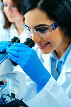 Young female scientist using microscope while her colleague working in Stock Photos