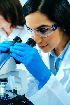 Young female scientist using microscope while her colleague working in Stock Photos
