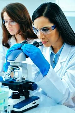 Young female scientist using microscope while her colleague working in Stock Photos