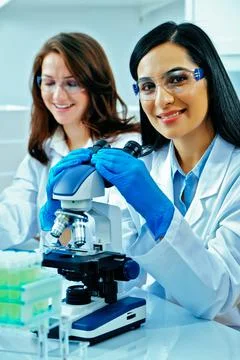 Young female scientist using microscope while her colleague working in Stock Photos