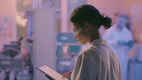 Young female senior scientist using digital tablet supervising team of 스톡 동영상 124303479