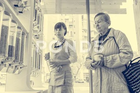 Young female shopkeeper helping elderly lady in zero waste store. Stock Photos