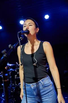 Young female singer performs vocal sound check on blue lit stage Stock Photos