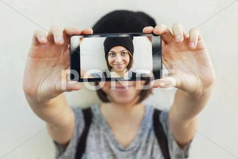 Young female skate boarder hiding behind smartphone with her selfie Stock Photos