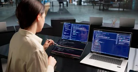 Young Female Software Developer Reviews Code Changes On Dual Touchscreen Lapt Stock Photos