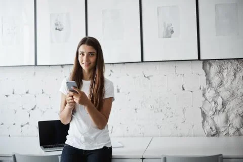 Young female software developer working remotely using smart phone and earphones Foto stock