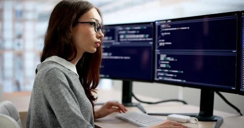 Young Female Software Engineer Intently Typing Code At Her Office Desk. Stock Photos