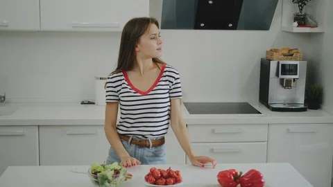A young female student is dancing in the kitchen and preparing herself a salad. 库存影片 111786023