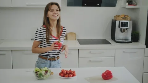 A young female student is dancing in the kitchen and preparing herself a salad. Stock Footage 111786236