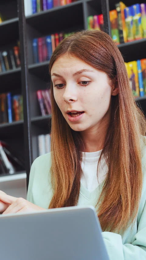 Young female student explaining idea during video call on laptop in library 스톡 동영상 341687648