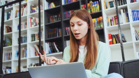 Young female student explaining material and counting on fingers in library 스톡 동영상 333331303