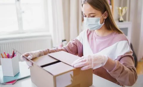 Young female student with face mask at the table, opening parcel box. Foto stock