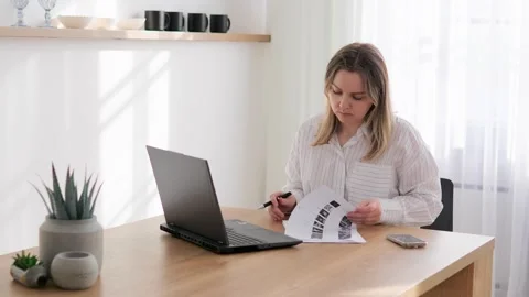 A young female student writes a lesson in a notebook while looking into a laptop Stock Footage 266972464
