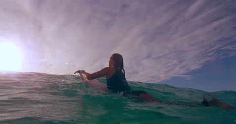 Young female surfer contemplating while lying on surfboard and swimming over an Stock Footage 199457380