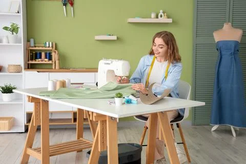 Young female tailor using sewing machine at table in atelier Stock Photos