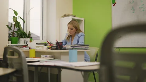 Young female teacher grading student tests in classroom, school work overload Stock Footage 333587041