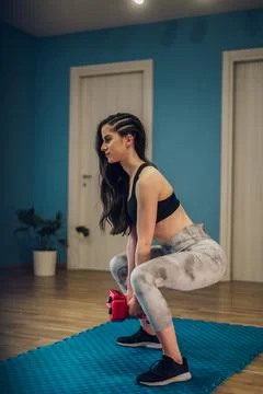 Young female training at home while doing squats and using dumbbells Stock Photos