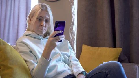 Young female user using mobile phone while sitting on sofa at home. Stock Photos