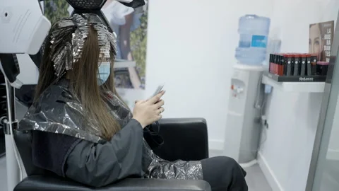 Young female using her phone while getting hair treatment at the salon in slow Video stock 205849078