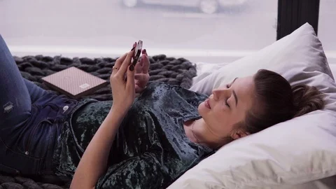 Young female using smartphone on bed by window Stock Footage 86086538
