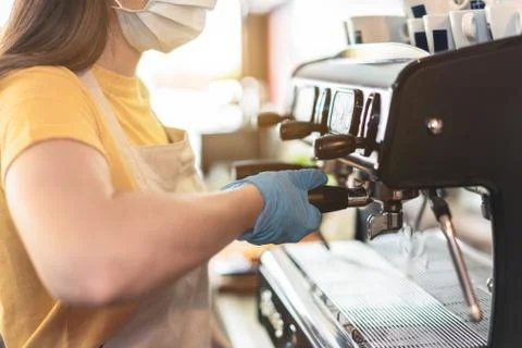 Young female working inside cafeteria bakery while making coffee wearing glov Stock Photos