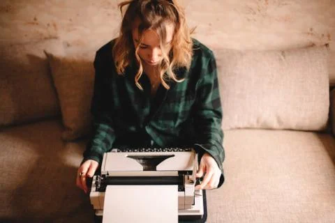 Young female writer using typewriter while sitting on sofa at home Stock Photos