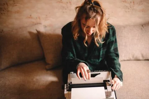 Young female writer using typewriter while sitting on sofa at home Stock Photos