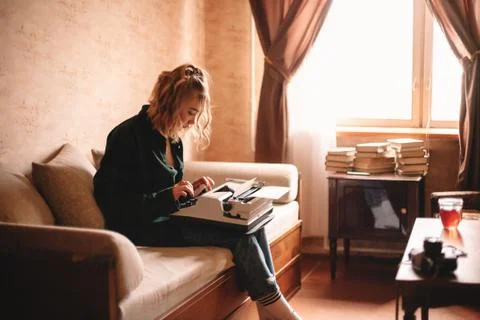 Young female writer using typewriter while sitting on sofa at home Stock Photos