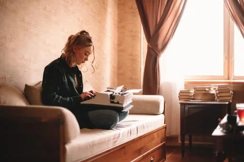 Young female writer using typewriter while sitting on sofa at home Stock Photos