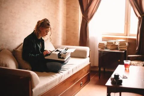 Young female writer using typewriter while sitting on sofa at home Stock Photos