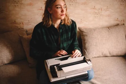 Young female writer using typewriter while sitting on sofa at home Stock Photos