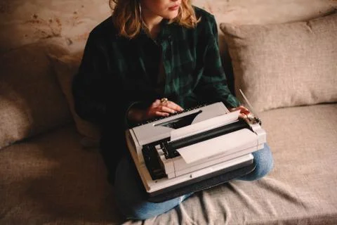 Young female writer using typewriter while sitting on sofa at home Stock Photos