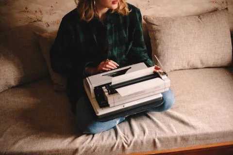Young female writer using typewriter while sitting on sofa at home Stock Photos