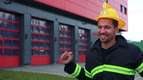 A young firefighter dances with a smile - a fire station in the background 動画素材 81205653