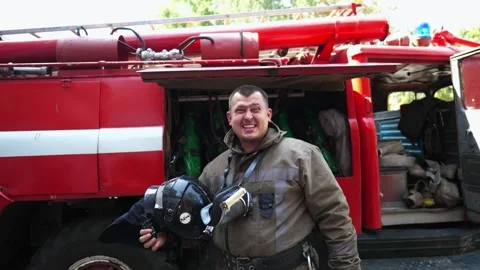 Young fireman taking off balaclava stands near fire engine. Male firefighter Stock Footage 275882054