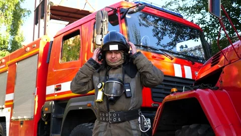 Young fireman taking off helmet and balaclava stands near fire engine Stock Footage 240847015