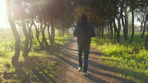 Young fit boy in black jacket running through the beautiful park on sunset. Видео 106731172