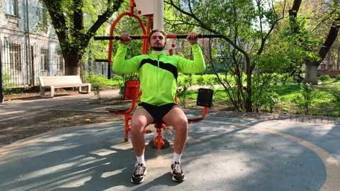 Young fit male using exercise machine and lifting his body in outdoor city gym Stockbeeldmateriaal 192060353