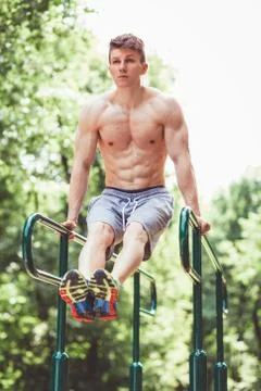 Young fit man doing push ups on bars Stock Photos