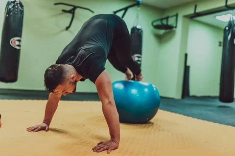 A young fit man doing push up plank exercise on medical ball at gym. Stock Photos