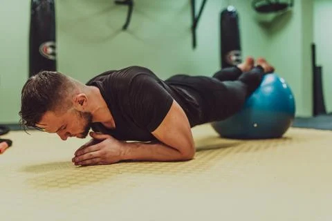 A young fit man doing push up plank exercise on ball at gym. Stock Photos