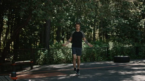 Young fit man jumping on rope in green city park Stock Footage 197293969